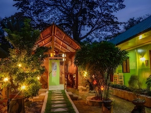 A traditional wooden structure with a thatched roof, surrounded by well-maintained greenery and a stone pathway leading to it. - Butterfly Totem Guesthouse (Puerto Princesa)