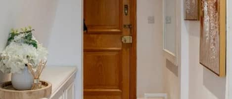 A hallway with a wooden door, a white bench, and a wall-mounted artwork.