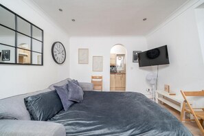 Een moderne slaapkamer met een groot bed, een flatscreen televisie en een eethoek zichtbaar door een boog.