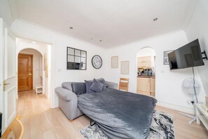 A modern bedroom with a bed, a sofa, a television, and a kitchen area. - Top-Floor 1-Bed Apt. in South Kensington (London)