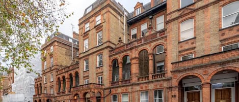 A row of red brick buildings with arched windows and a central entrance.