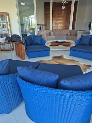 A modern living room with blue wicker furniture, a glass coffee table, and a leather sofa.