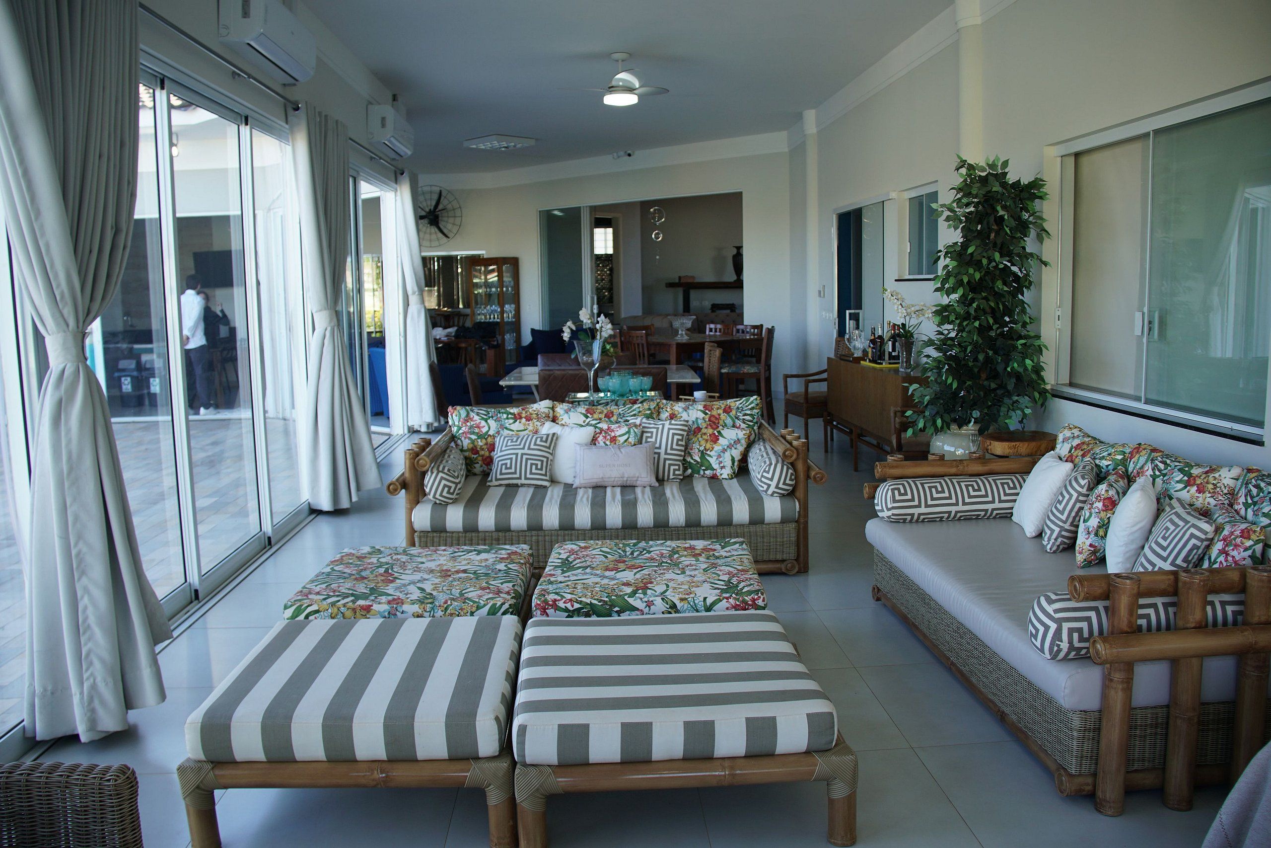 A spacious living area with a sofa set, a dining table, and a large window with curtains.