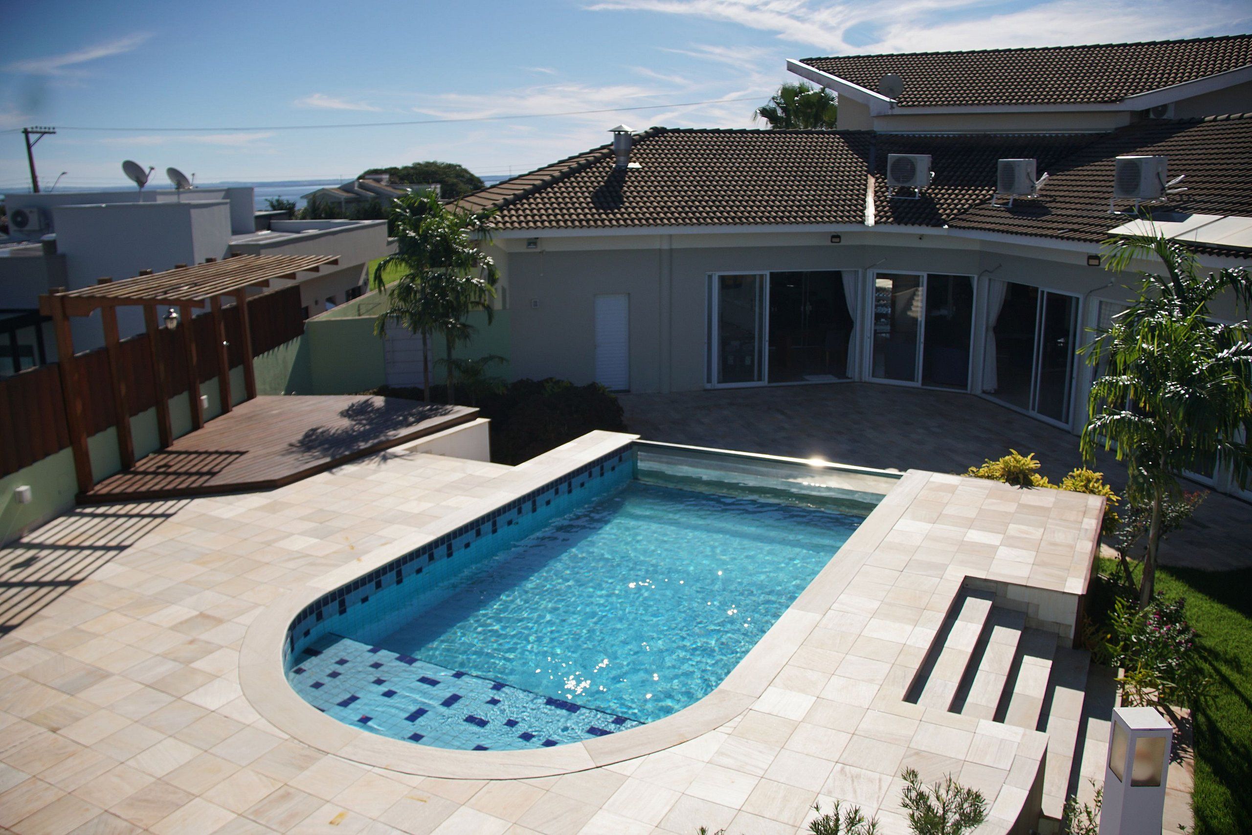 Una piscina de borde curvo, rodeada por un patio con suelo de baldosas.