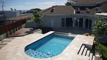 Una piscina de borde curvo, rodeada por un patio con suelo de baldosas.