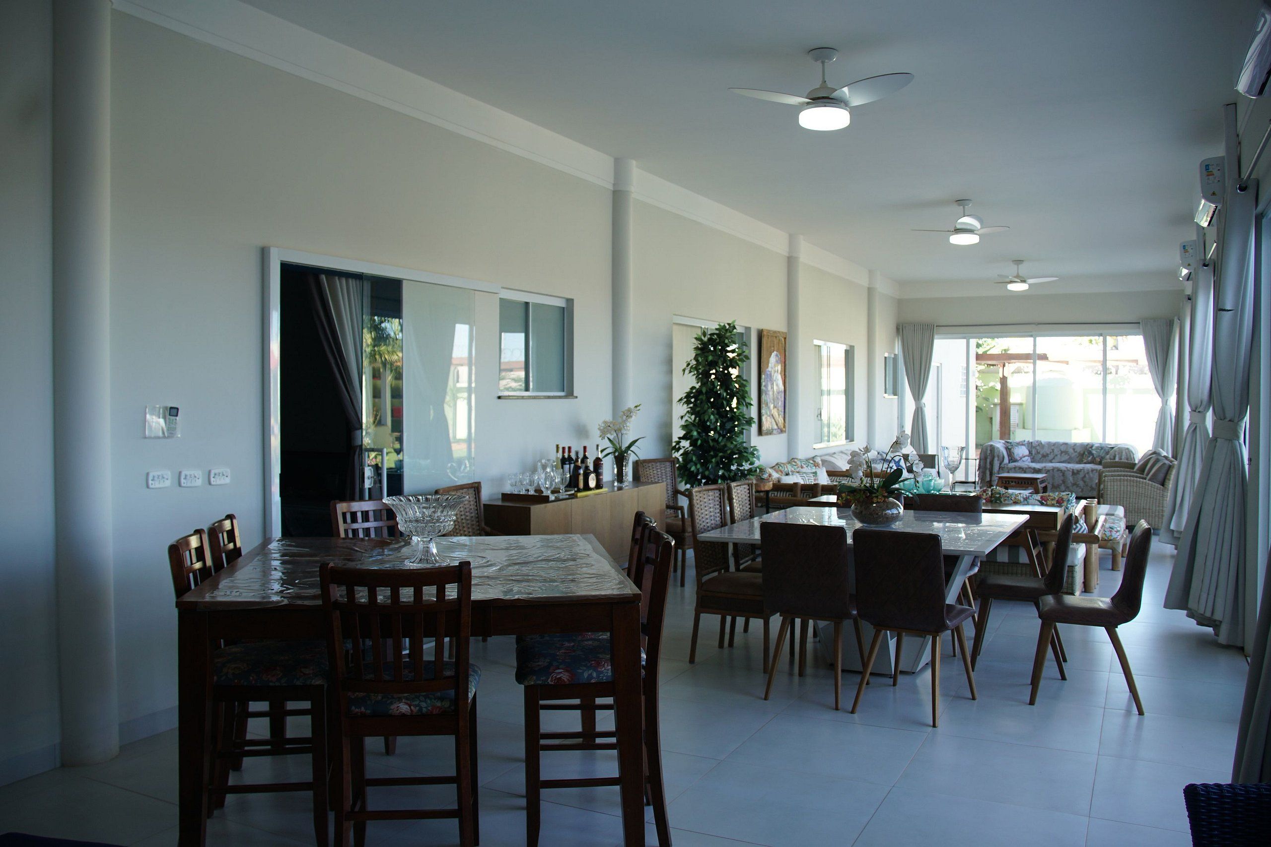 Une salle à manger spacieuse avec un grand ventilateur de plafond, une grande fenêtre avec des rideaux et une vue sur l’extérieur.