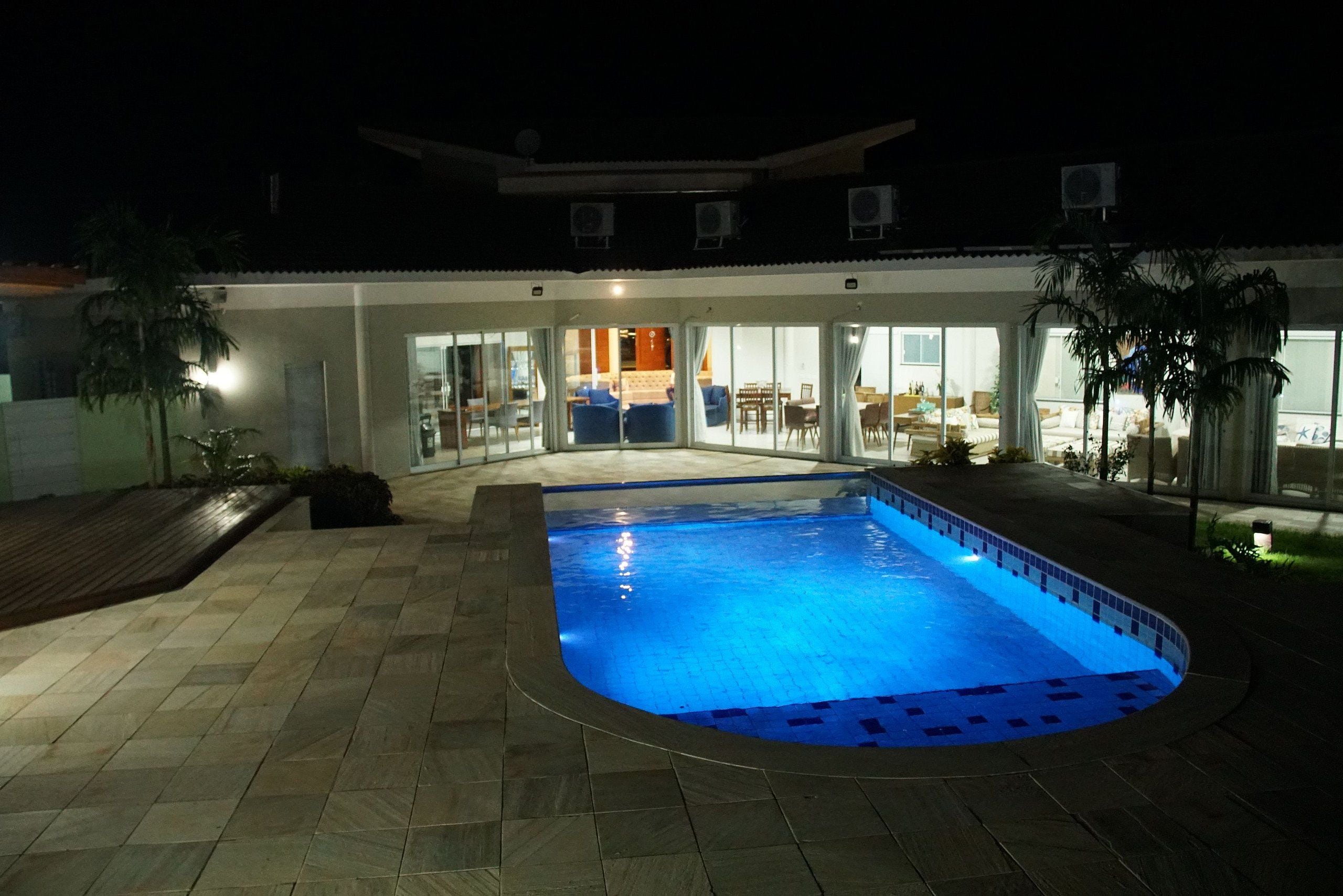 A swimming pool with a tiled deck, a covered patio area, and a view into the building.