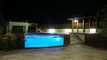 Piscina com borda iluminada, pérgola de madeira e escadaria para um segundo andar.