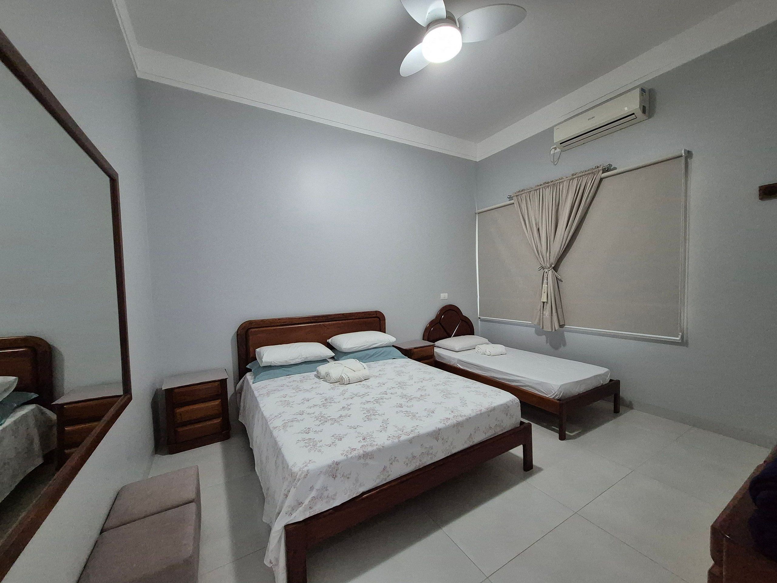 A bedroom with two single beds, a wooden headboard, a bedside table, a mirror, and an air conditioning unit.