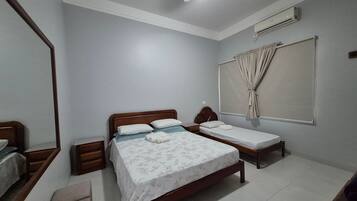 Quarto com duas camas de solteiro, cabeceira de madeira, mesa de cabeceira, espelho e ar condicionado.