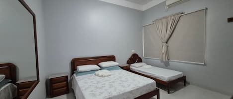 A bedroom with two single beds, a wooden headboard, a bedside table, a mirror, and an air conditioning unit.