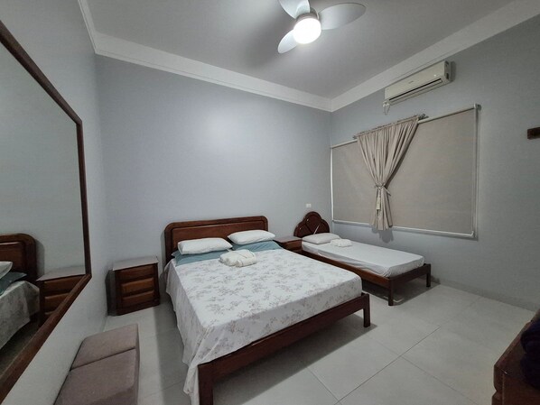 A bedroom with two single beds, a wooden headboard, a bedside table, a mirror, and an air conditioning unit.