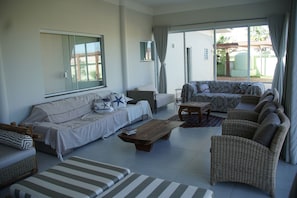 A spacious living area with a sofa, armchairs, a coffee table, and a large sliding glass door leading to an outdoor patio.