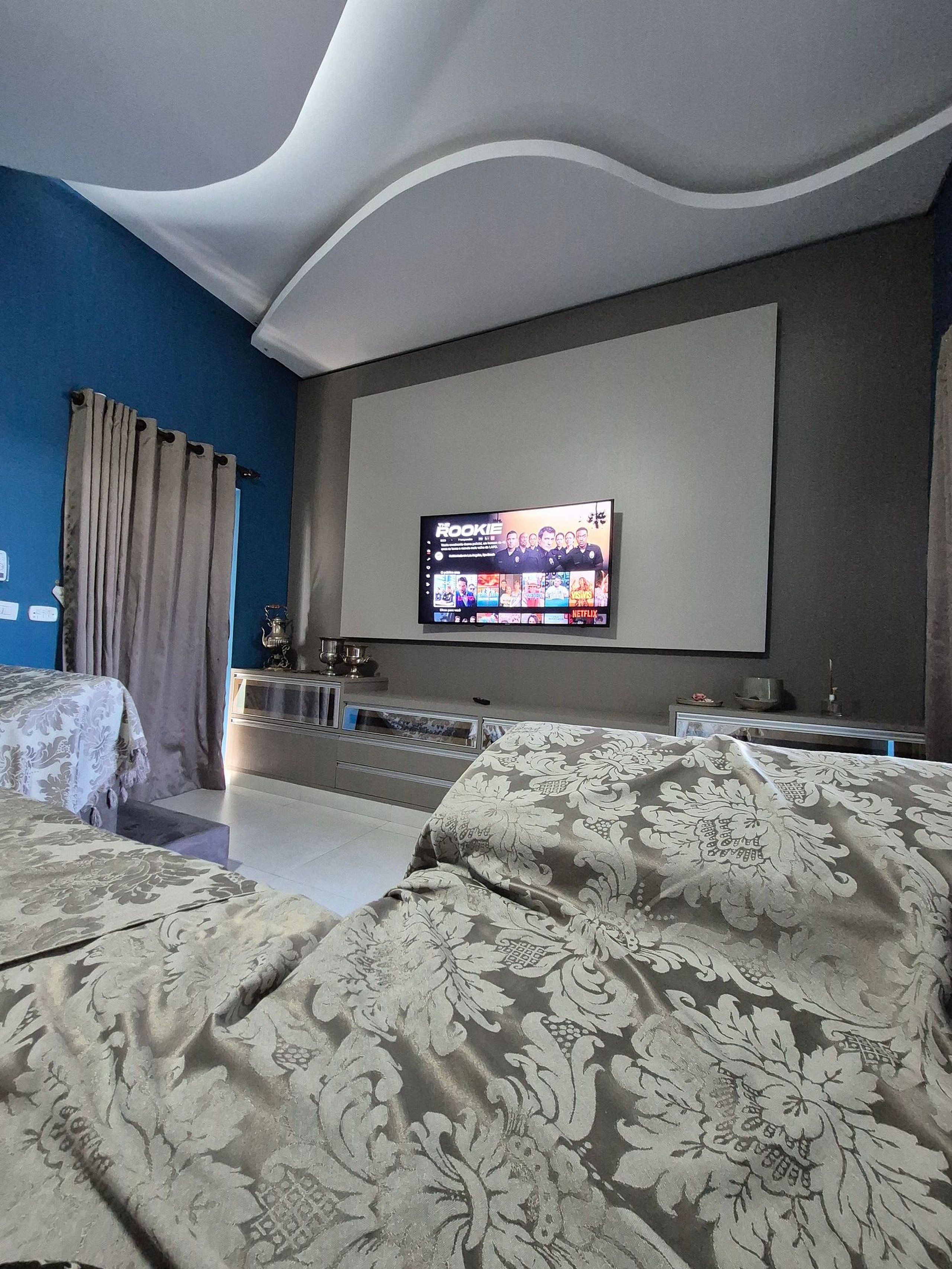 Hotelkamer met een grote flatscreen televisie aan de muur, een bed met beddengoed met een patroon, een klein tafeltje met decoratieve objecten, en een trap die naar een hoger niveau leidt.
