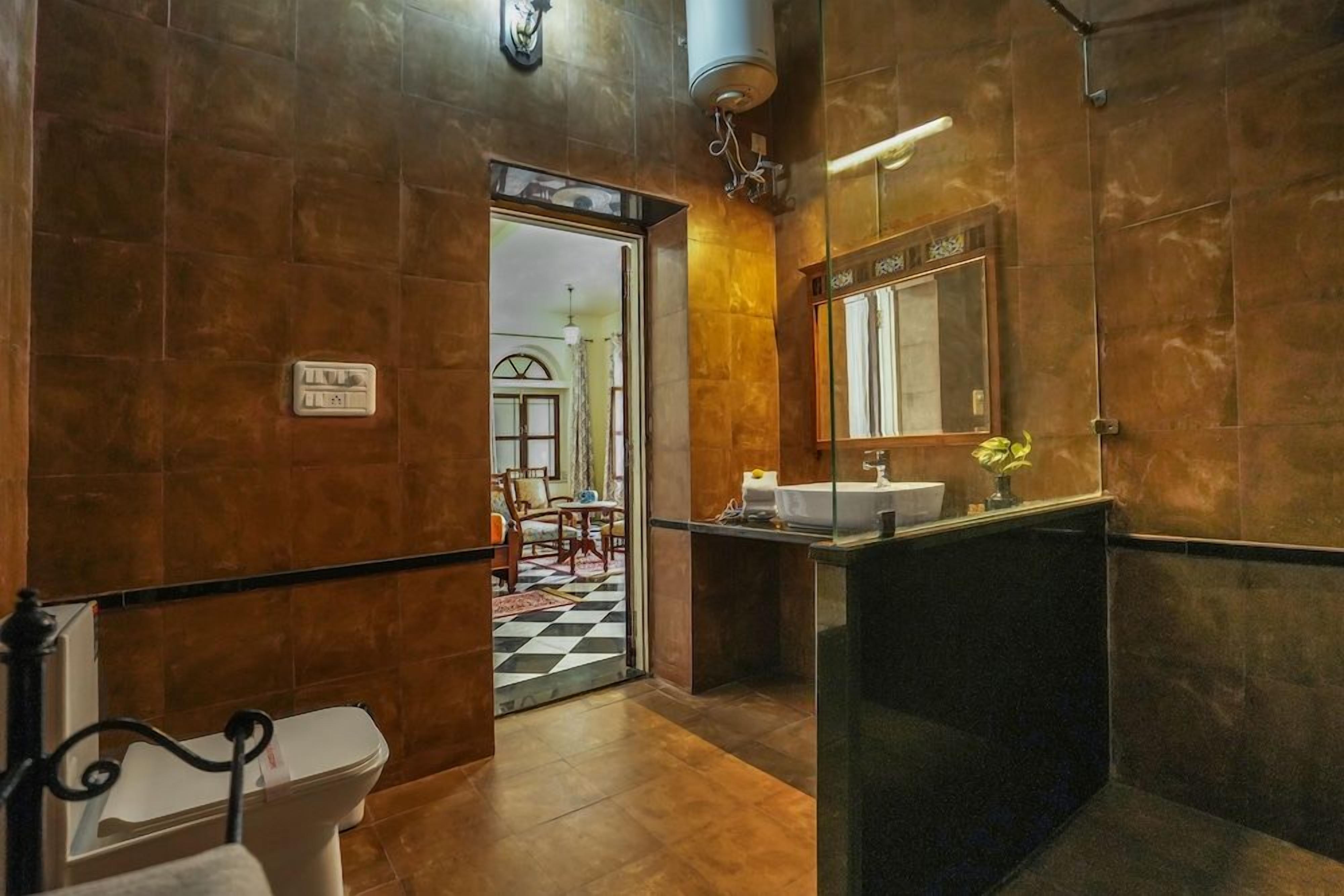A bathroom with a toilet, sink, and mirror. There is a door leading to a dining area.