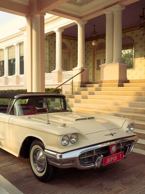 Une voiture ancienne est garée devant un bâtiment orné de colonnes et d’un escalier.