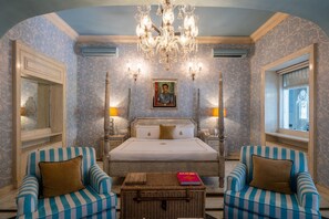 Une chambre à coucher avec un lit à baldaquin, deux fauteuils rembourrés, un lustre et un tableau accroché au mur.