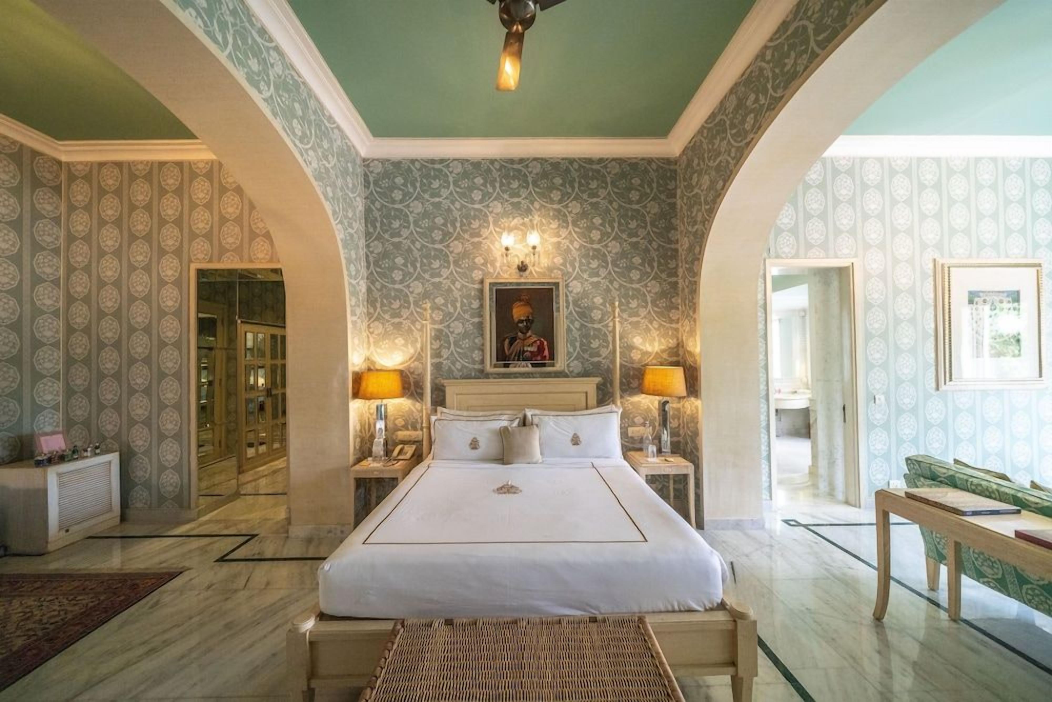 Habitación de hotel con una cama grande, dos mesitas de noche, un sofá verde y un papel tapiz estampado.