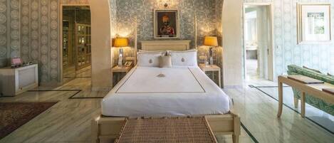 Habitación de hotel con una cama grande, dos mesitas de noche, un sofá verde y un papel tapiz estampado.