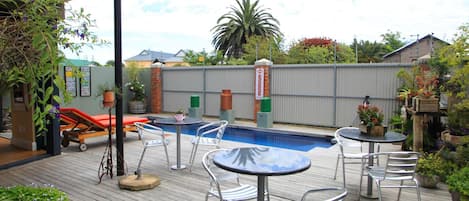 An outdoor pool area with lounge chairs, a table, and potted plants.