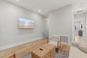 A modern living room with a flat-screen TV mounted on the wall, a wooden coffee table, a striped armchair, and a patterned rug.