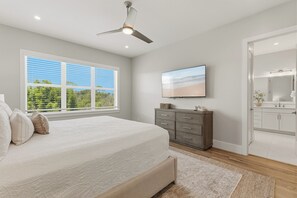 A bedroom with a bed, dresser, TV, and a window with blinds.