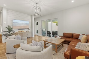 Ein modernes Wohnzimmer mit einem Flachbildfernseher, einem braunen Ledersofa und einem weißen Sessel.