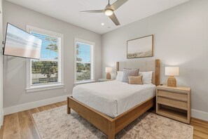 Ein Schlafzimmer mit einem Bett, zwei Nachttischen inklusive Lampen, einem Deckenventilator und zwei Fenstern mit Jalousien.