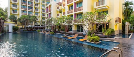 Un hotel con piscina, varios balcones y abundante vegetación.