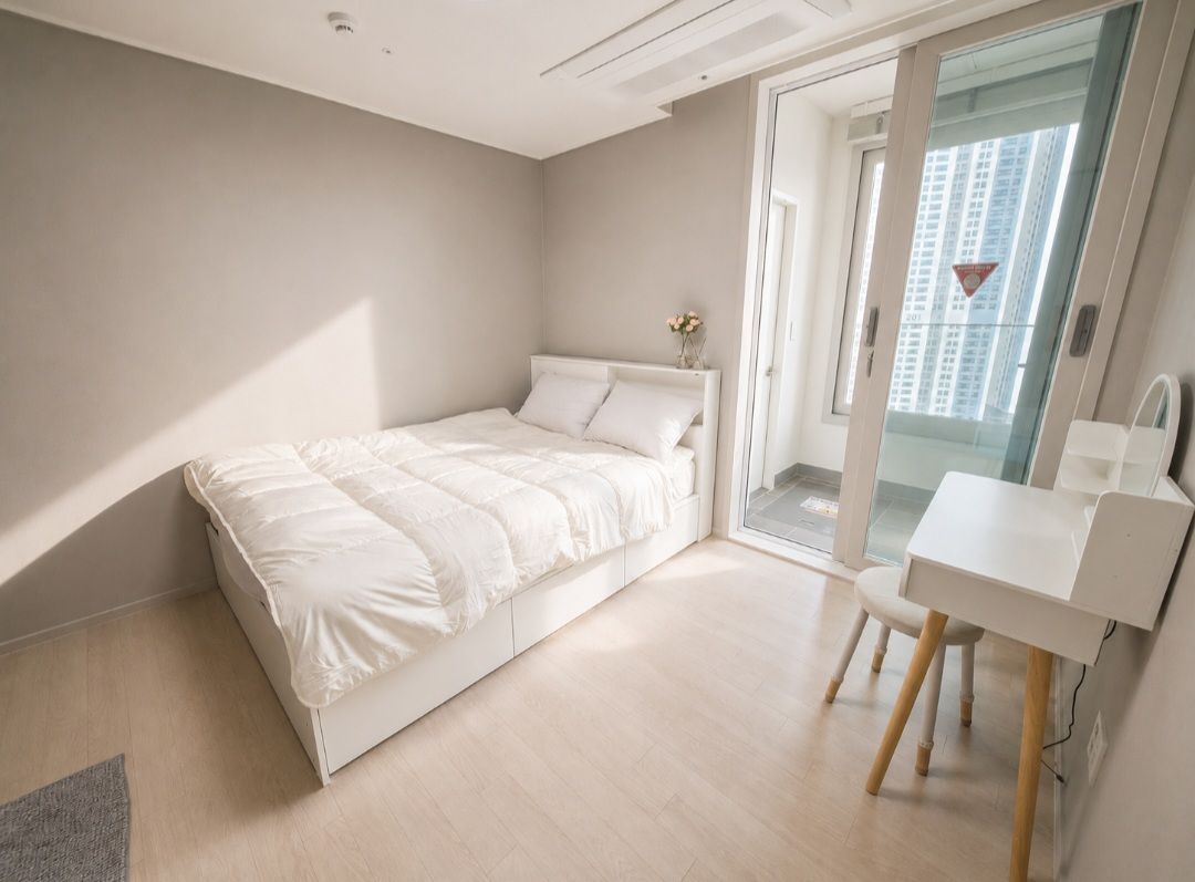 A bedroom with a bed, a desk, and a view of a building through a glass door.