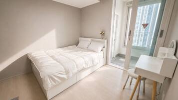 A bedroom with a bed, a desk, and a view of a building through a glass door.