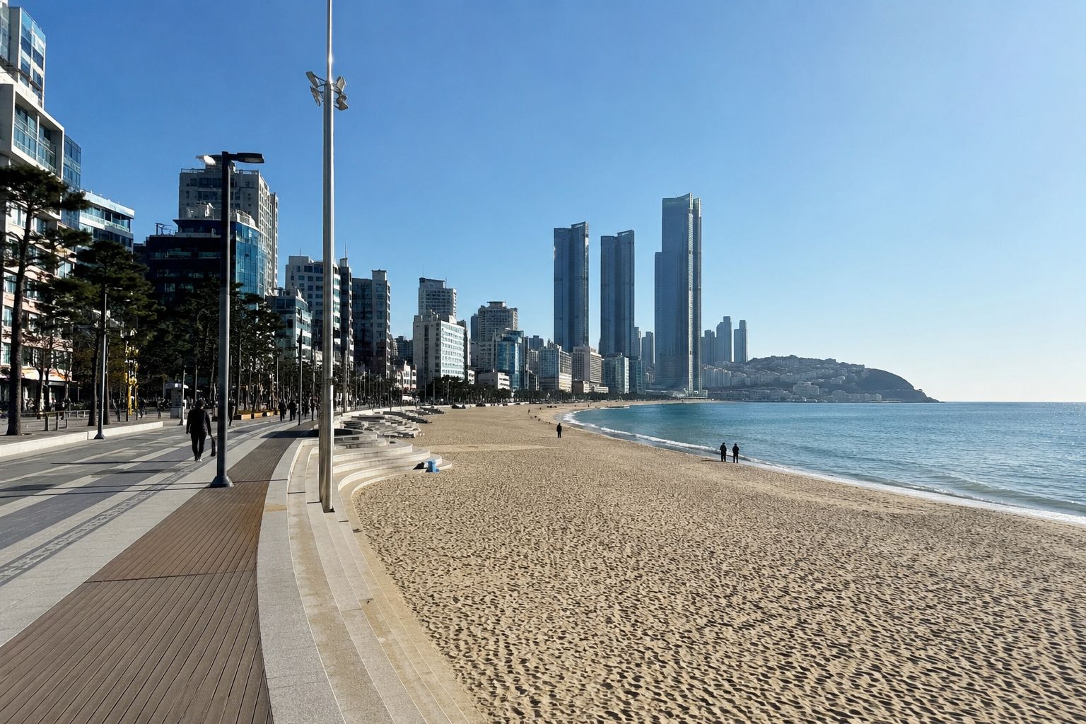 A beach with a promenade, tall buildings, and a clear sky.