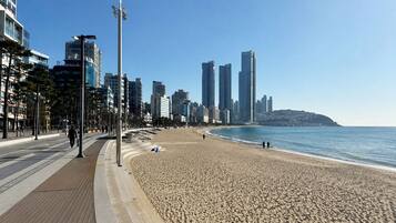A beach with a promenade, tall buildings, and a clear sky.
