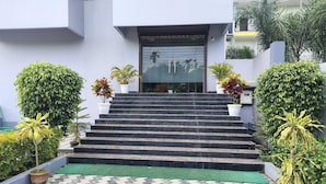 Un conjunto de escaleras exteriores que conducen a la entrada de un edificio, rodeado de plantas en macetas y un pavimento con diseño.
