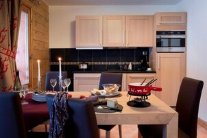 Un coin repas avec une table dressée pour deux personnes, un set à fondue rouge et un plan de travail noir avec une cuisinière.