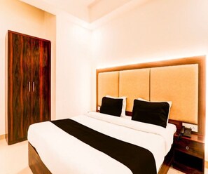 A hotel room with a large bed, a wooden wardrobe, and a nightstand with a phone. - Deluxe the yug Residency (Varanasi)