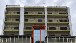Ein mehrstöckiges Gebäude mit einem zentralen Eingang, Balkonen und einer gläsernen Fassade.