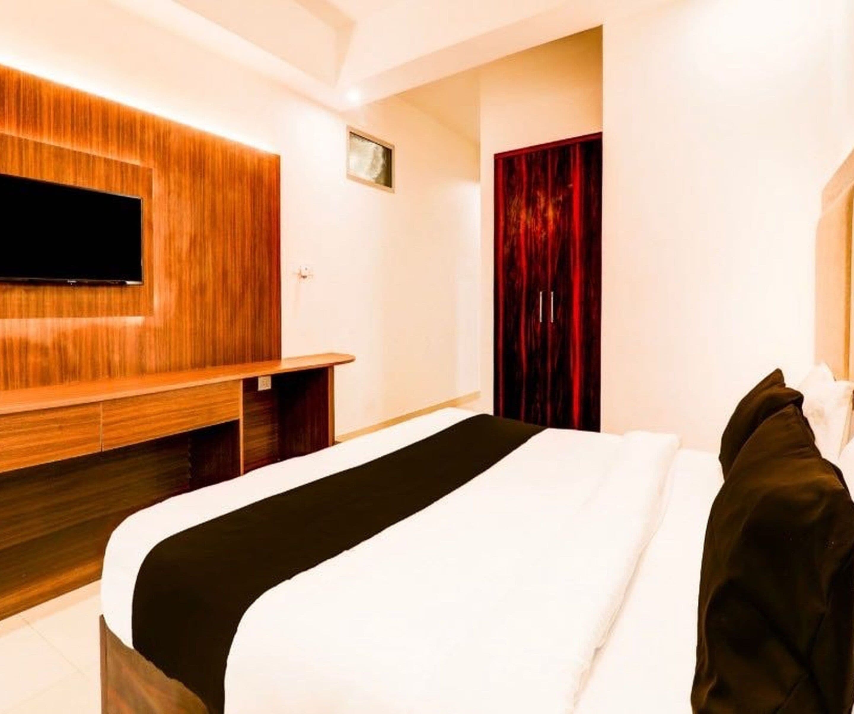 A hotel room with a bed, a TV mounted on the wall, and a wardrobe.