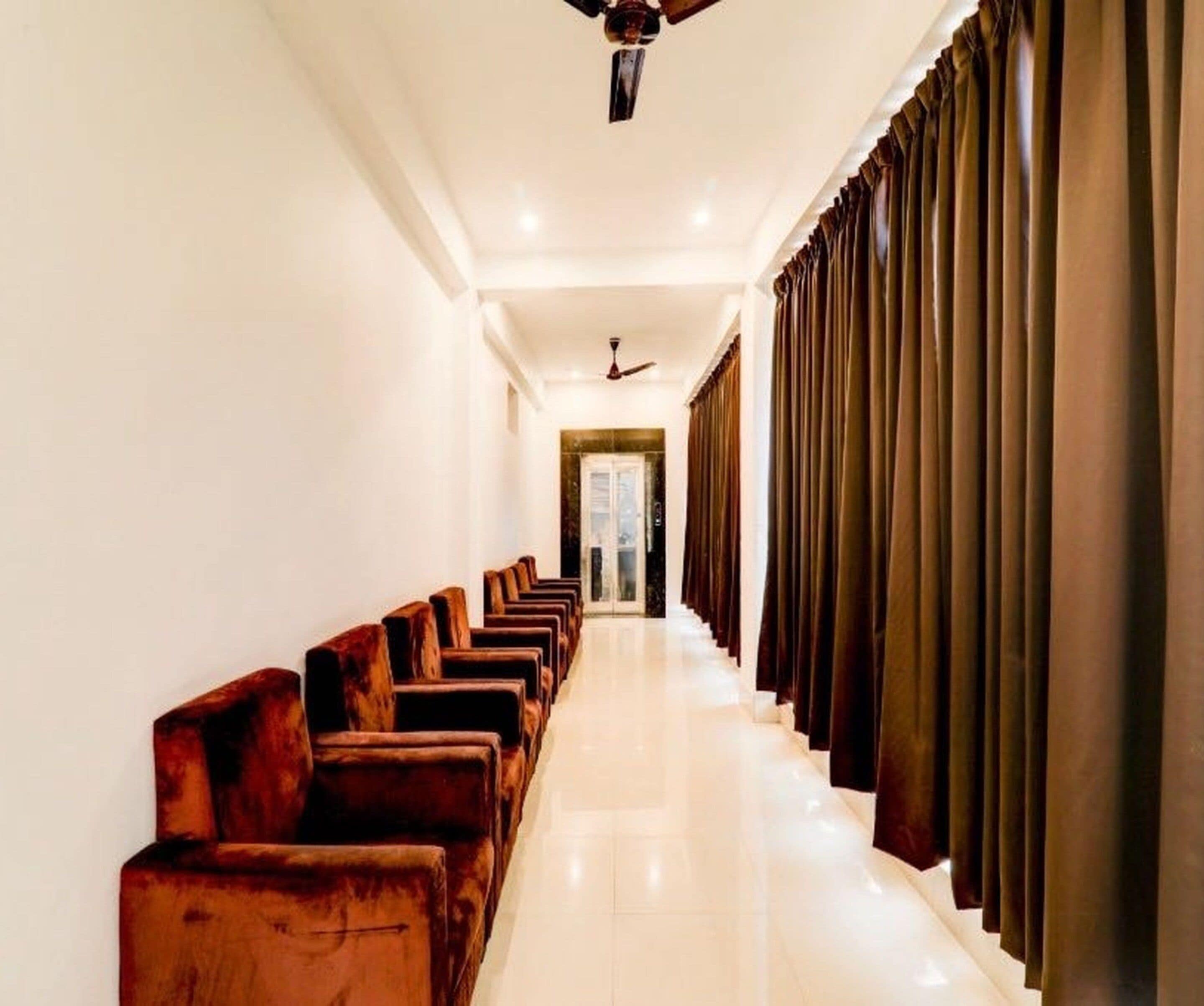 A hotel corridor with rows of wooden chairs, a ceiling fan, and a door at the end.
