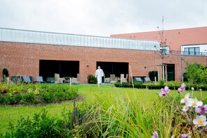 A building with a brick facade, large open garage doors, and a grassy area with outdoor seating.