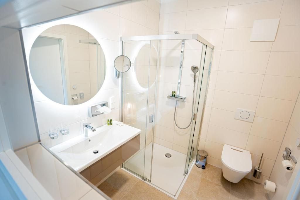Un baño moderno con ducha envuelta en vidrio, un espejo redondo y un lavamanos blanco.