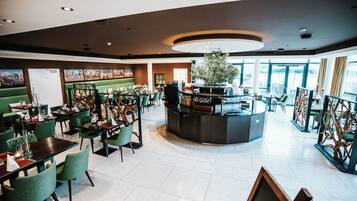 Un amplio hall de hotel con un mostrador de recepción central, zonas de estar verdes y grandes ventanales que aportan luz natural.