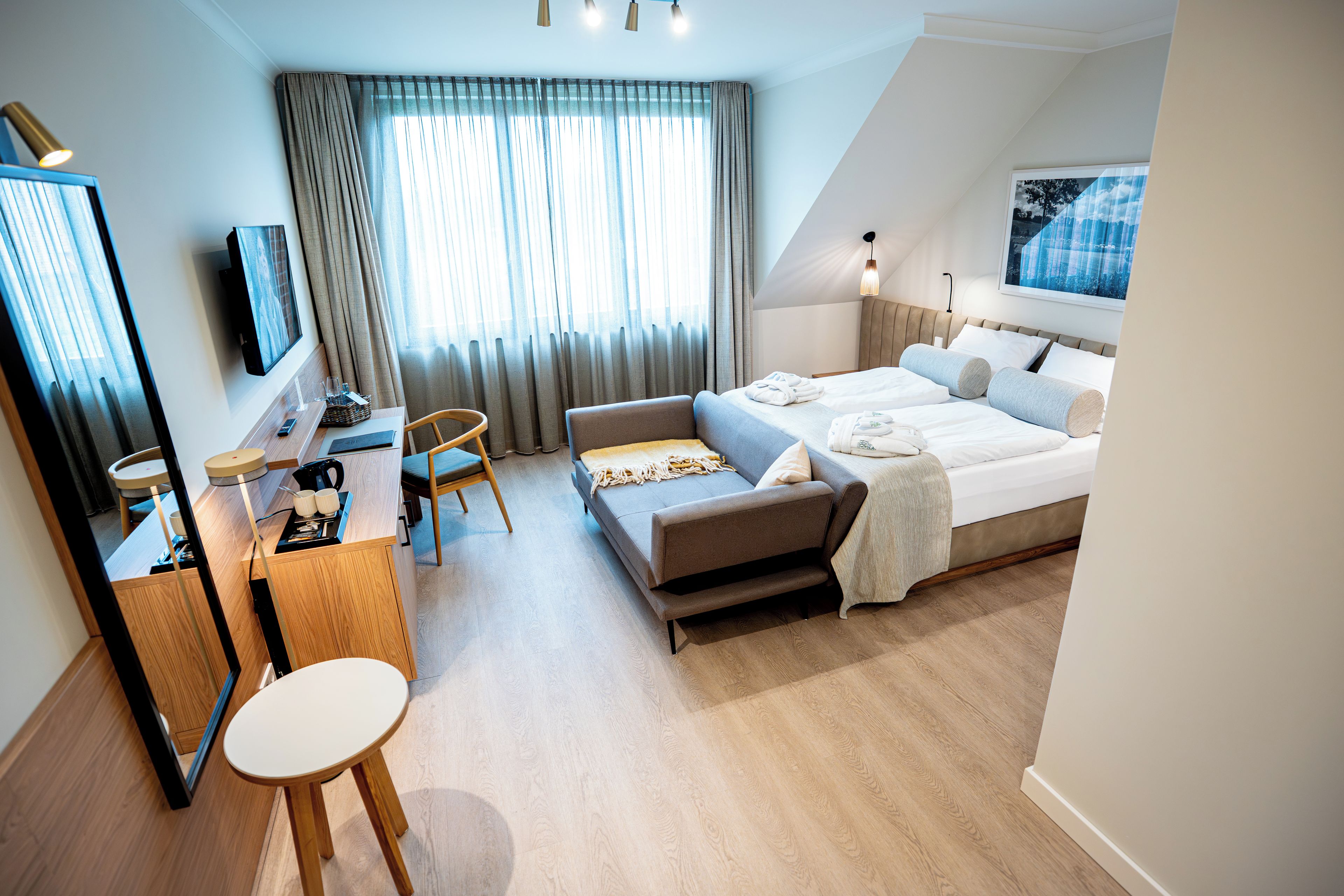 A modern hotel room with a bed, a desk, a chair, and a large window with curtains.
