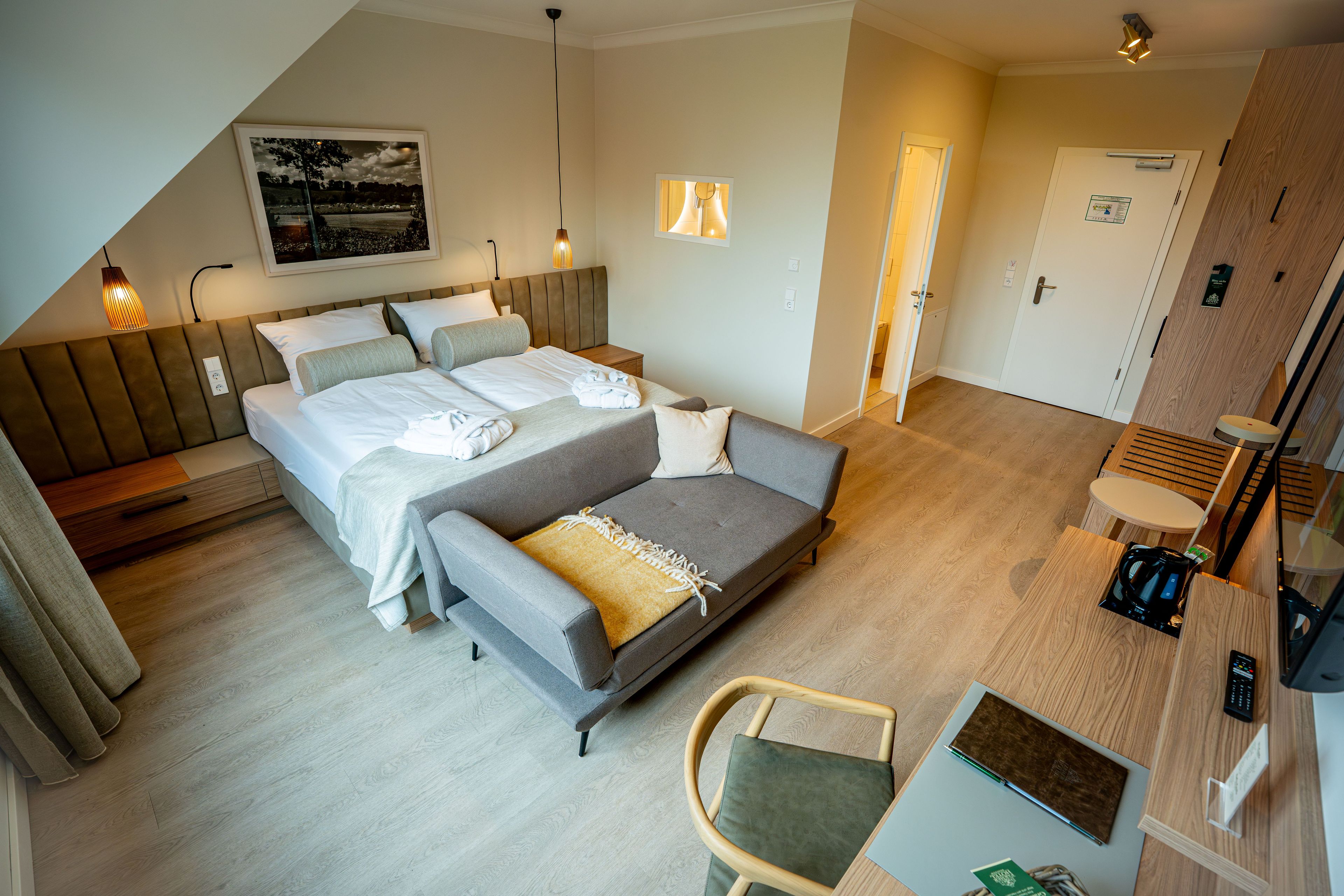 A modern hotel room with a bed, a sofa, a chair, a desk, and a coffee machine.