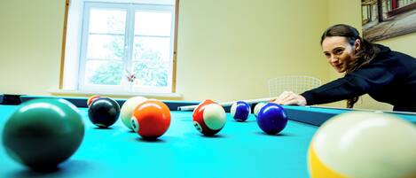 Une table de billard avec des billes, dans une pièce dotée d’une fenêtre et d’un tableau au mur.