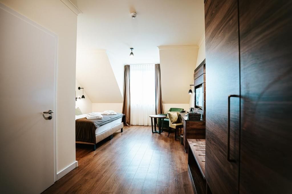 A hotel room with a bed, a desk, a chair, a small table, and a wardrobe.