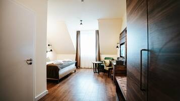 A hotel room with a bed, a desk, a chair, a small table, and a wardrobe.