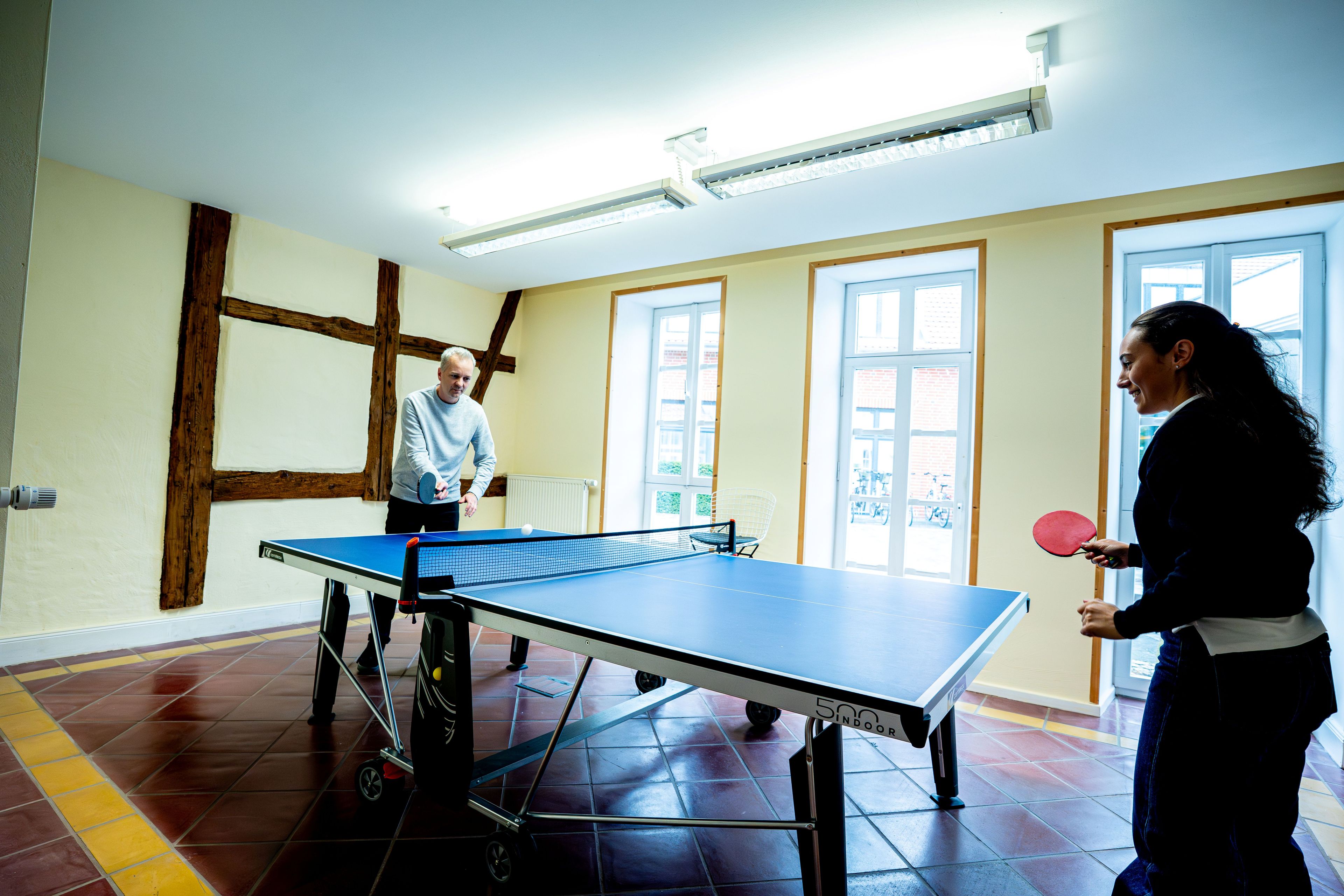 A ping pong table in a room with a tiled floor, a window, and a door.