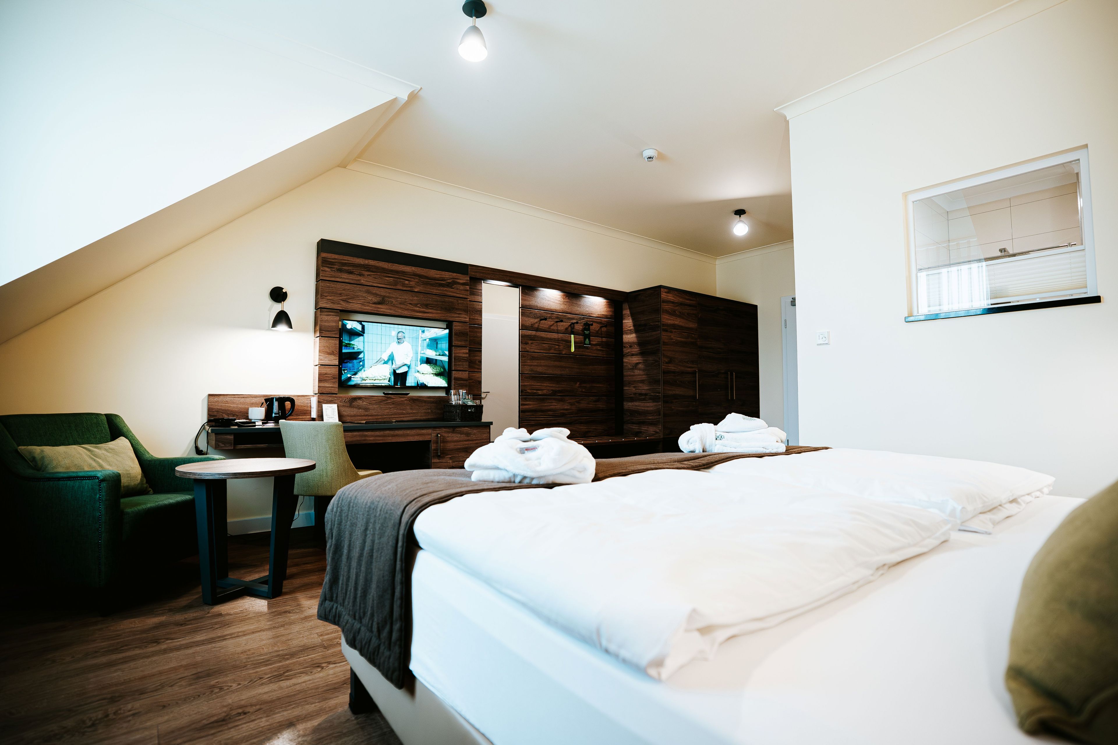 Una habitación de hotel con cama, escritorio, silla, televisor y una pared de madera decorativa.