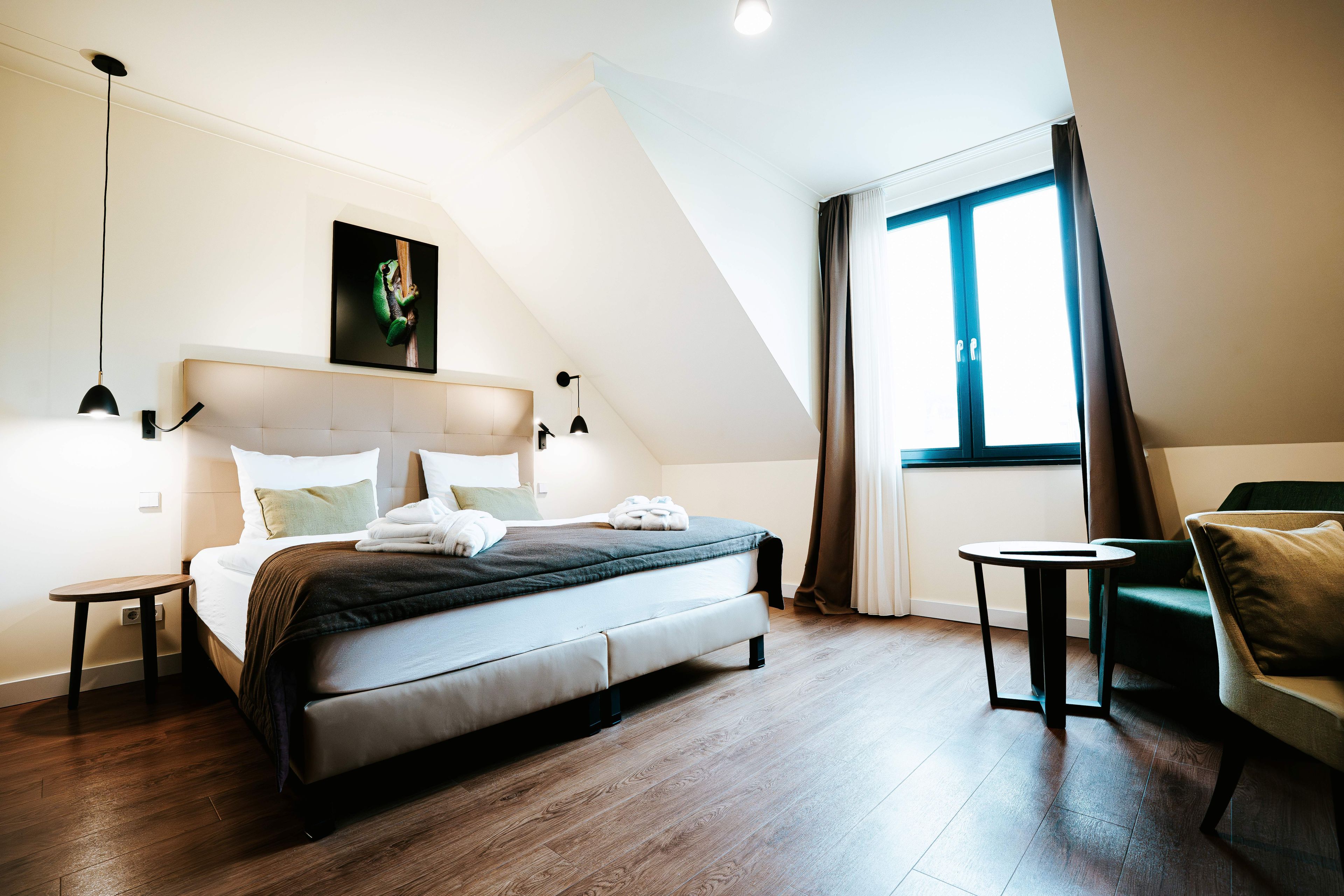 Un dormitorio moderno con cama, una mesita de noche, una silla, una ventana con cortinas y un cuadro en la pared.